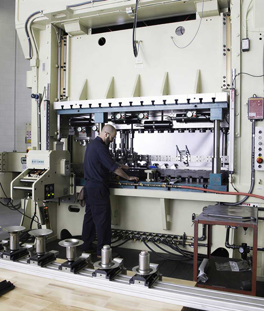 Large industrial metal stamping press being operated by a worker at Stewart EFI.