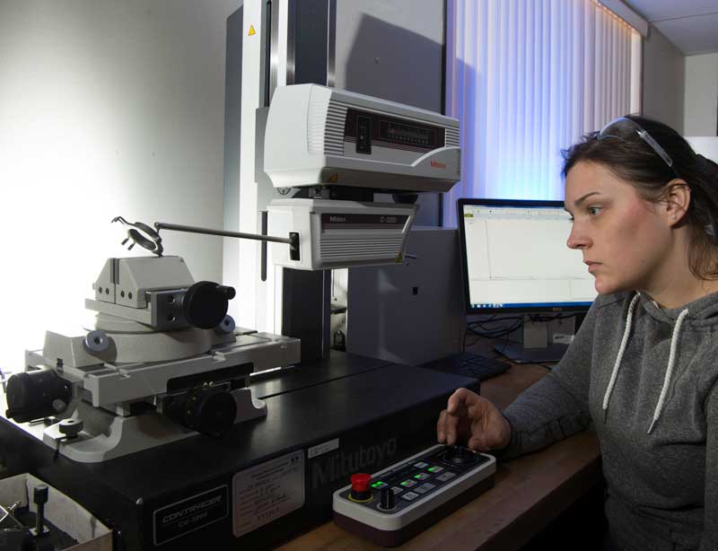 Quality inspector operating a Mitutoyo contour measurement system to analyze a precision metal part.