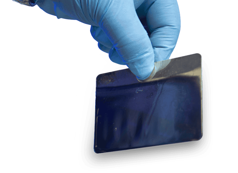 Gloved hand holding a thin stamped metal plate with a formed edge.