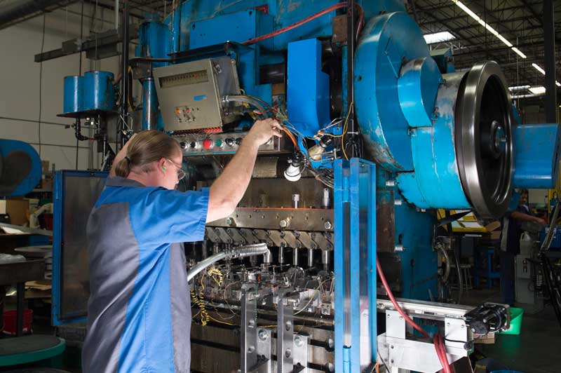 Manufacturing technician adjusting wiring and controls on a large industrial metal stamping press in a factory.