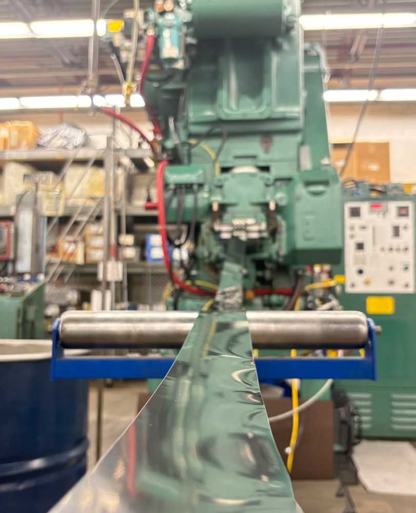 Metal strip feeding into a high-speed stamping press inside an industrial manufacturing facility.