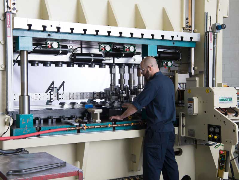 Manufacturing technician operating a large metal stamping press machine on a factory floor.