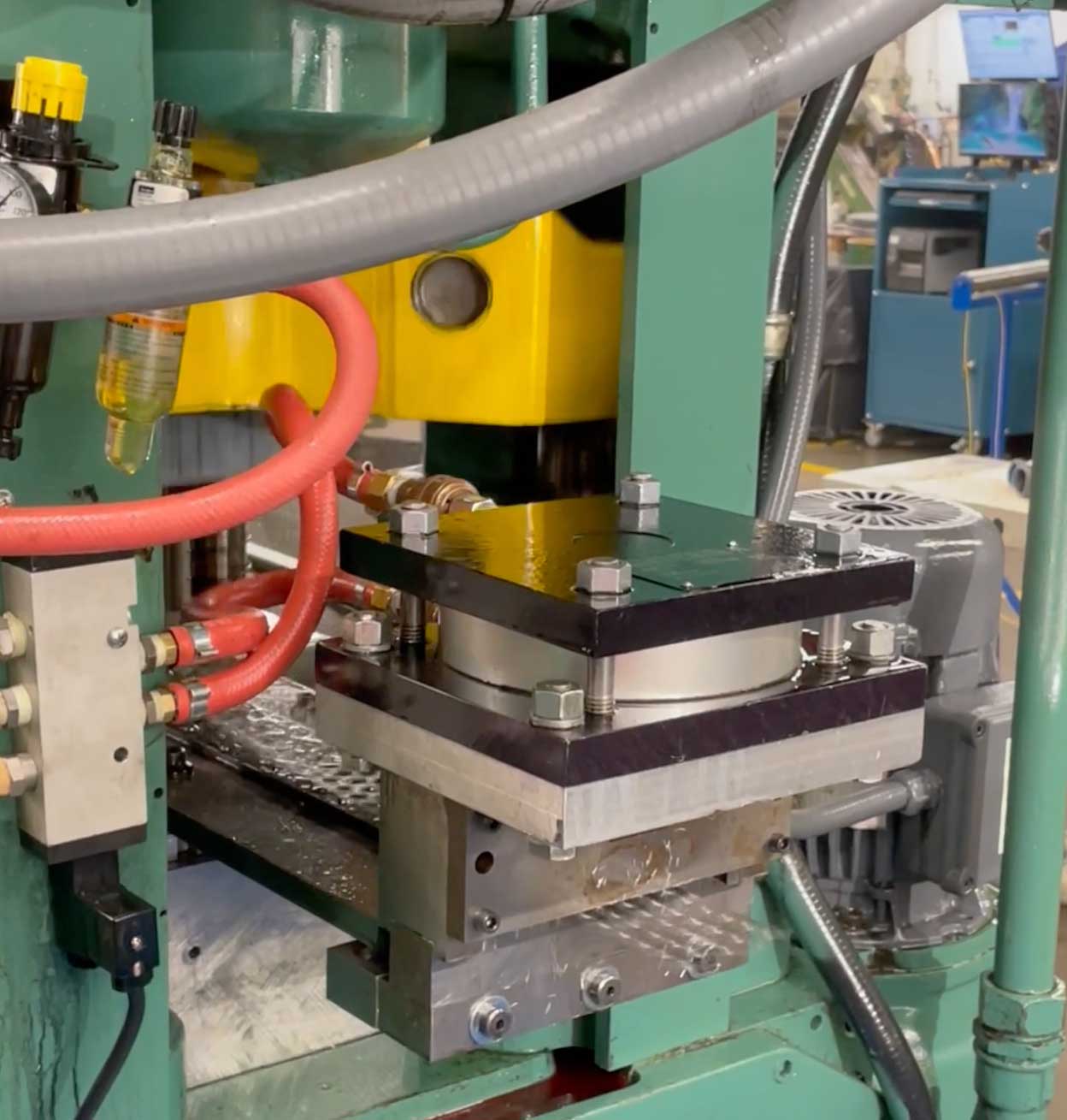 Close-up of industrial hydraulic press tooling with hoses and fittings inside a metal forming machine.